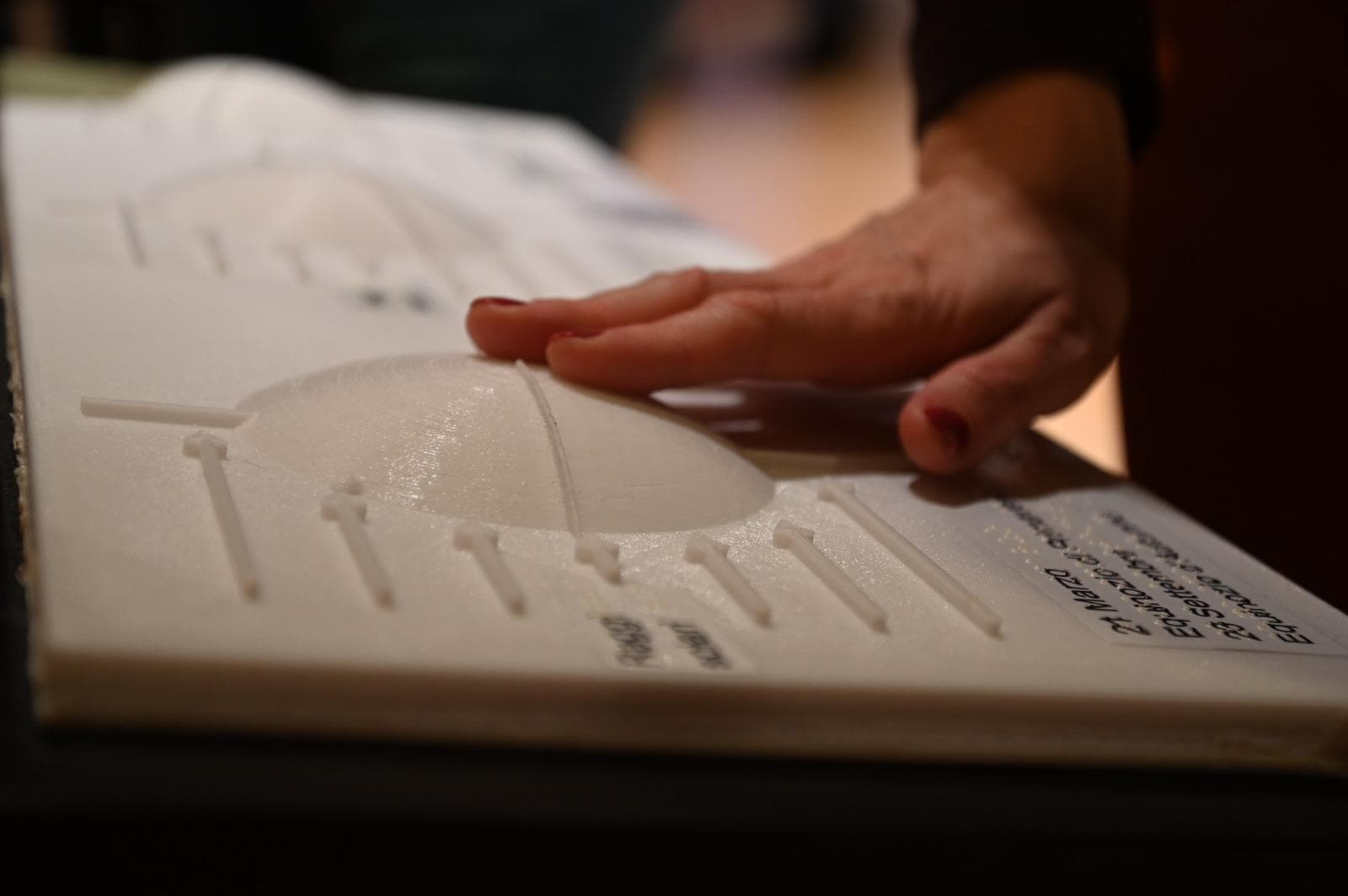 Una mano sfiora un pannello tattile in rilievo con una cupola e simboli in Braille, durante un laboratorio multisensoriale di astronomia